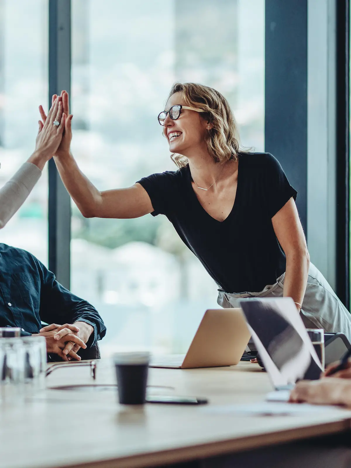 Female professional giving a high five to her colleague in conference room. Group of colleagues celebrating success in a meeting.