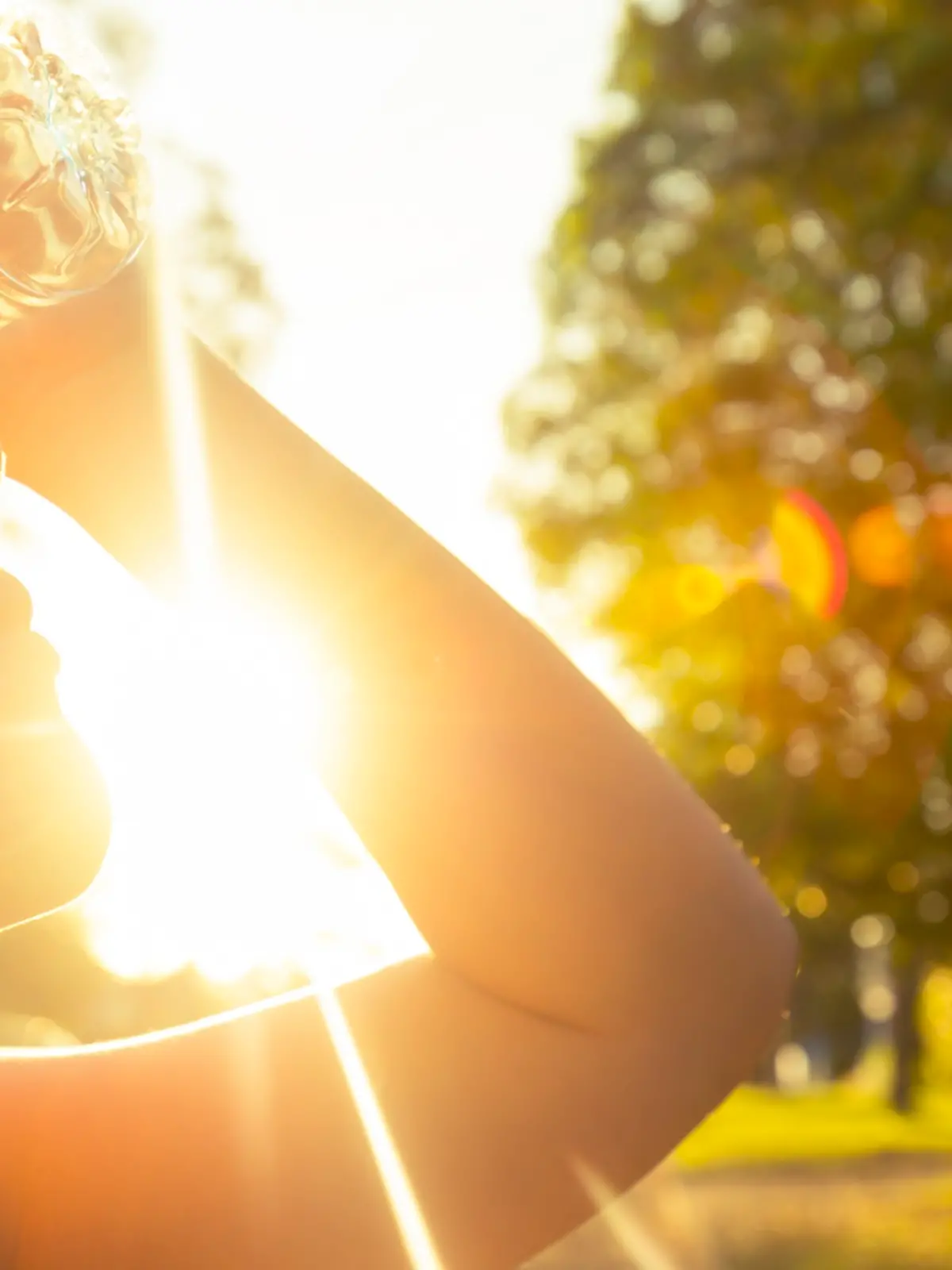 Woman using water bottle to cool down. Fitness and wellbeing concept with female athlete cooling down on a city street. She is holding a water bottle to her head to cool down. The sun is low creating long shadows and some lens flare. Copy space