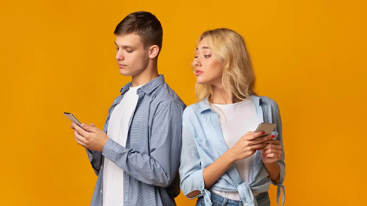 Mistrust concept. Curious young girl peeking over shoulder how her boyfriend texting on phone, panorama with free space