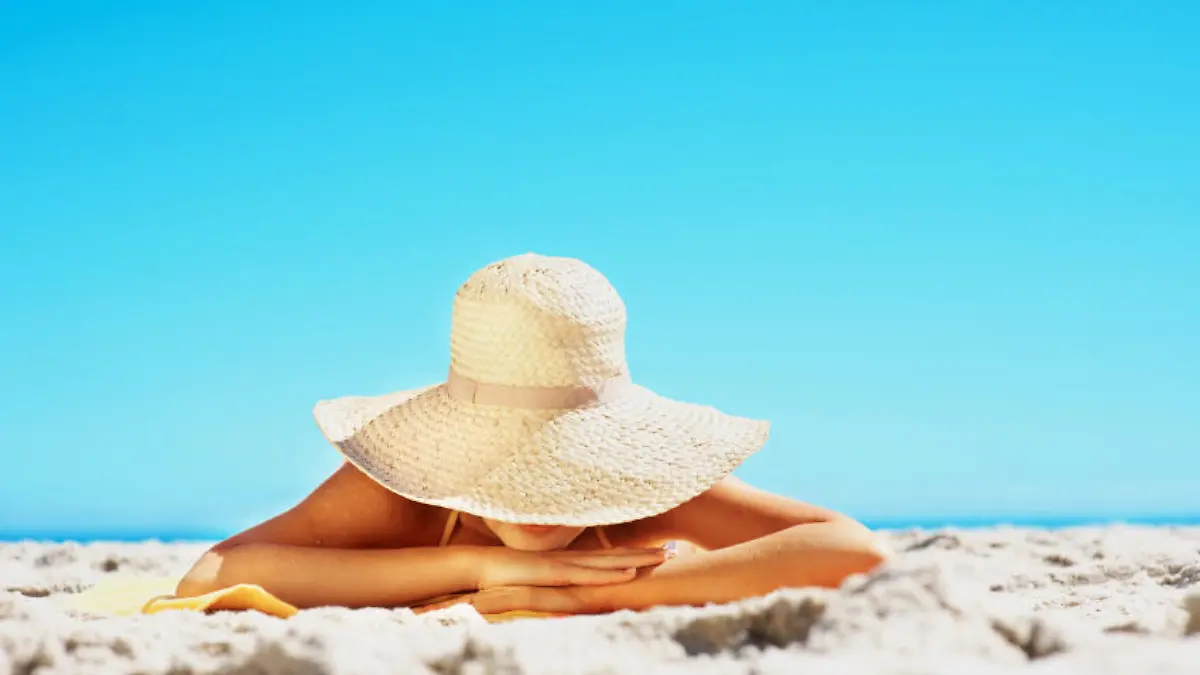 Woman lying on sandy beach in a big sun hat with copy space against clear blue sky