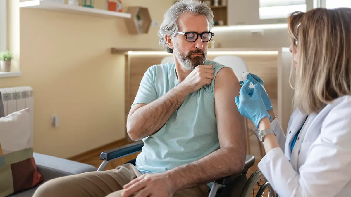 Disabled Male Patient Sitting in the Wheelchair Getting Vaccinated at His Home by Female Doctor