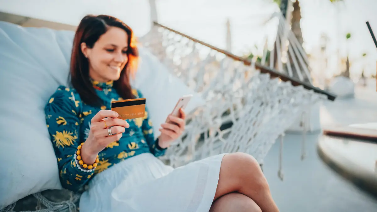 Relaxed woman in hammock using credit card for online shopping
