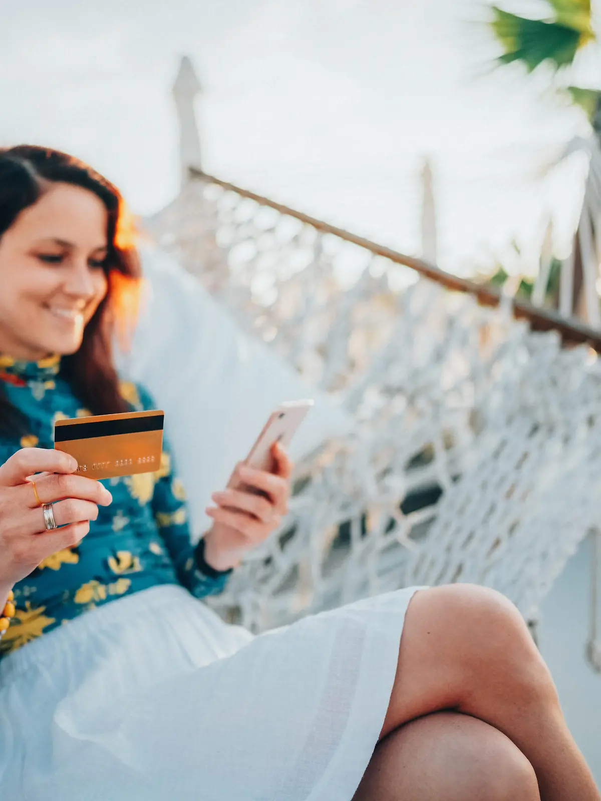 Relaxed woman in hammock using credit card for online shopping