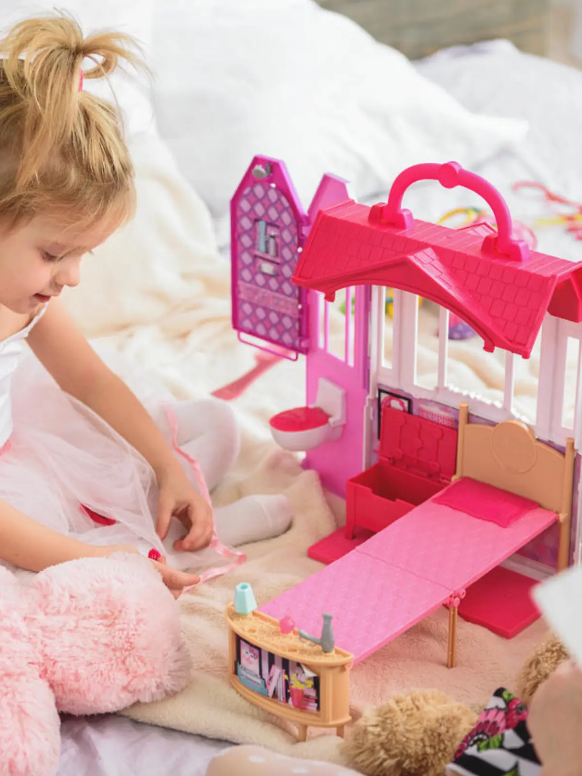 Pretty little child is enjoying game in doll house with her elder sister. She is sitting on bed and smiling