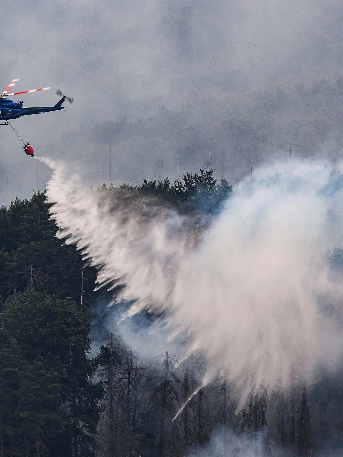 26.07.2022, Tschechien, Hrensko: Mit einem Hubschrauber wird ein Waldbrand im tschechischen Nationalpark Böhmische Schweiz in Hrensko nahe der Grenze zu Sachsen gelöscht. Der Brand breitet sich im Nationalpark Sächsische Schweiz aus. Foto: Robert Michael/dpa +++ dpa-Bildfunk +++