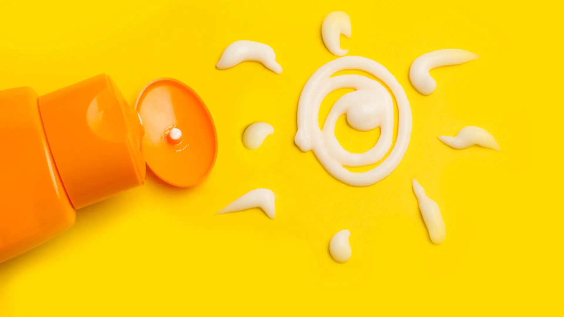 A sun cream protection bottle with a sun drawed with cream on a yellow background