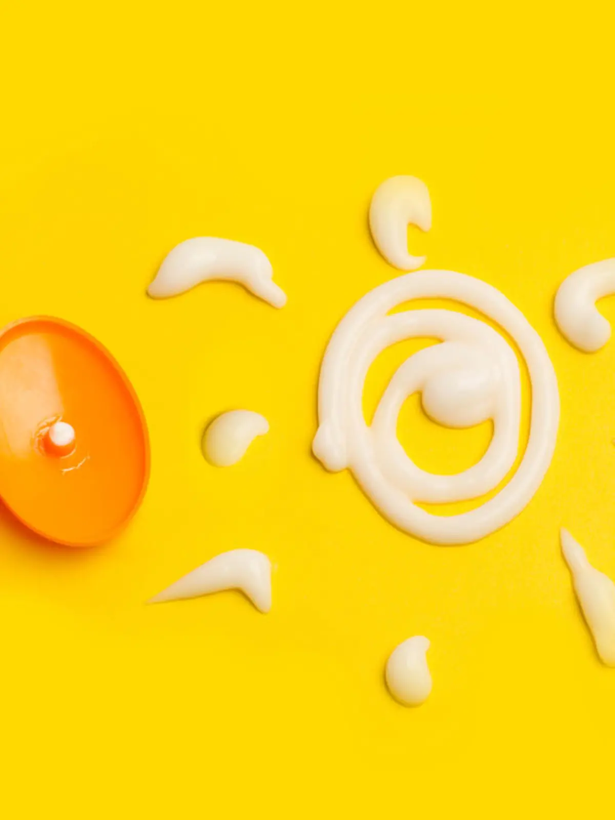 A sun cream protection bottle with a sun drawed with cream on a yellow background