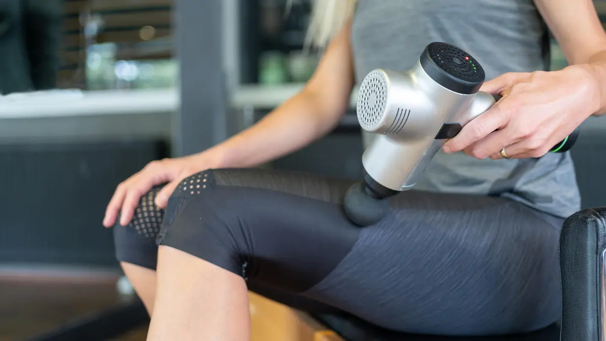 Woman Massaging Leg With Massage Gun After Exercising In Pilates Studio