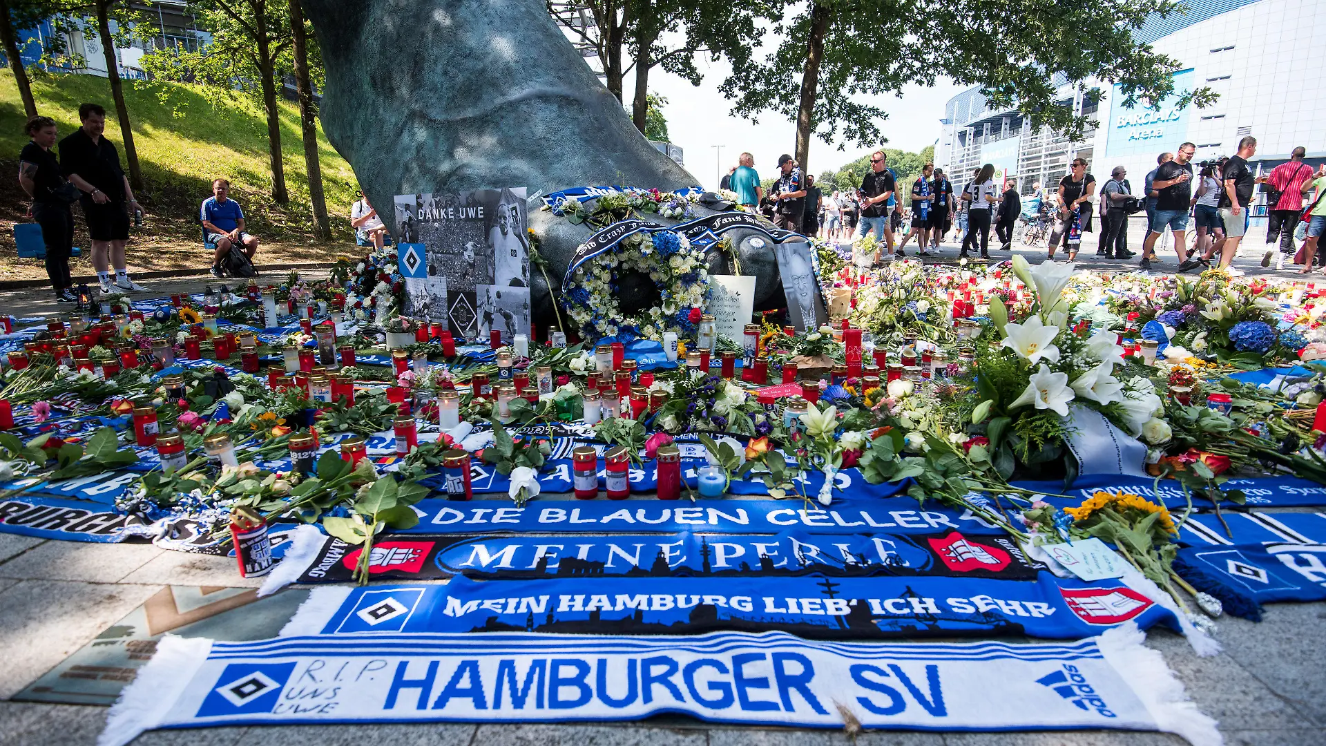 24.07.2022, Hamburg: Zahlreiche Blumen, Kerzen und Schals liegen und stehen vor dem Fußball-Zweitligaspiel Hamburger SV - Hansa Rostock vor einer Bronze vor dem Volksparkstadion, die den Fuß des ehemaligen Fußballspielers Uwe Seeler abbildet. Seeler ist im Alter von 85 Jahren gestorben. Foto: Daniel Bockwoldt/dpa - WICHTIGER HINWEIS: Gemäß den Vorgaben der DFL Deutsche Fußball Liga bzw. des DFB Deutscher Fußball-Bund ist es untersagt, in dem Stadion und/oder vom Spiel angefertigte Fotoaufnahmen in Form von Sequenzbildern und/oder videoähnlichen Fotostrecken zu verwerten bzw. verwerten zu lassen. +++ dpa-Bildfunk +++