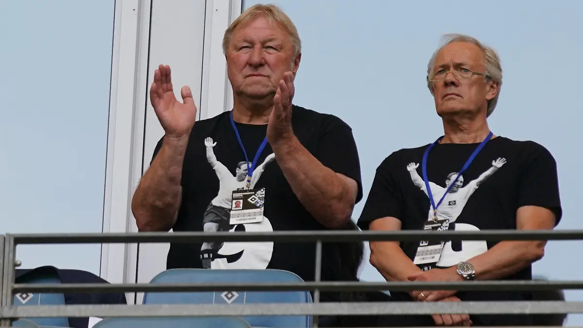 24.07.2022, Hamburg: Fußball: 2. Bundesliga, 2. Spieltag, Hamburger SV - Hansa Rostock, im Volksparkstadion. Horst Hrubesch (l) und Bernd Wehmeyer stehen auf der Tribüne und tragen T-Shirts in Gedenken an Uwe Seeler. Foto: Marcus Brandt/dpa - WICHTIGER HINWEIS: Gemäß den Vorgaben der DFL Deutsche Fußball Liga bzw. des DFB Deutscher Fußball-Bund ist es untersagt, in dem Stadion und/oder vom Spiel angefertigte Fotoaufnahmen in Form von Sequenzbildern und/oder videoähnlichen Fotostrecken zu verwerten bzw. verwerten zu lassen. +++ dpa-Bildfunk +++