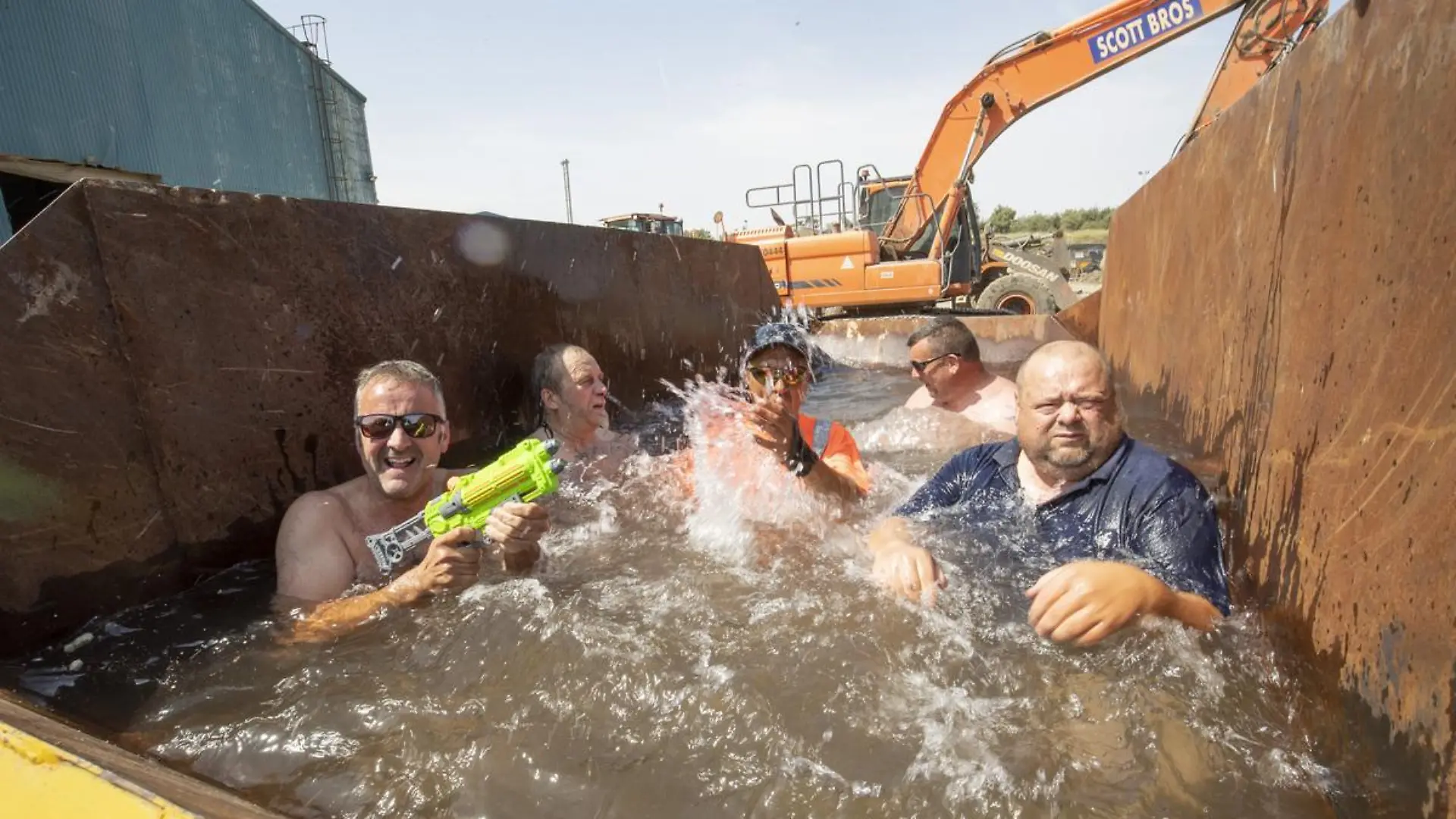 Story from Jam Press (Swimming Pool Skip)
Pictured: Employees at Scott Bros enjoying their improvised swimming pool.
‘Almost as good as Benidorm!’: Workers turn rusty SKIP into swimming pool to cool off in summer
A company in Stockton took matters into their own hands this week in a bid to help cool down its employees – by turning one of their rusty skips into a makeshift swimming pool.
As temperatures reached a scorching 38 degrees in Teeside earlier this week, employees at Scott Bros, a family-run large haulage and plant hire business, were desperate for a way to cool down as they worked away in the heat.
Peter Scott, 46, company director, took matters into his own hands and decided to fill one of their empty skips with water.
"It might look a little strange, but a large skip makes the perfect plunge pool," Peter told NeedToKnow.online.
"We had no shortage of people asking if they could take a quick dip.
"It was also a bit of fun, while allowing people a well-deserved break.
"It really helped our staff to completely cool down."
To ensure the skip was safe for employers, the company cleaned it out with a pressure washer and inserted plastic sheeting in the bottom.
As a recycling firm, they then filled up the skip with recycled water from their bowser.
Peter said: "Everyone really loved it, partly because at heart we are a recycling firm, and we were following the company ethos by taking an empty skip and repurposed it as a plunge pool!
"There was plenty of mickey taking and laughter, but those who took a turn really enjoyed themselves.
"We even found a couple of squirter guns to add to the fun.”
Neil Crawford, a machine operator at Scott Bros, was one of the employees who took the plunge.
He said: “We’ve been happy to get on with our jobs despite the heat, but this is a proper treat.
"It’s almost as good as being by the pool in Benidorm!”
Peter has said that a lot of people have dismissed the creativity as a "stunt" but says