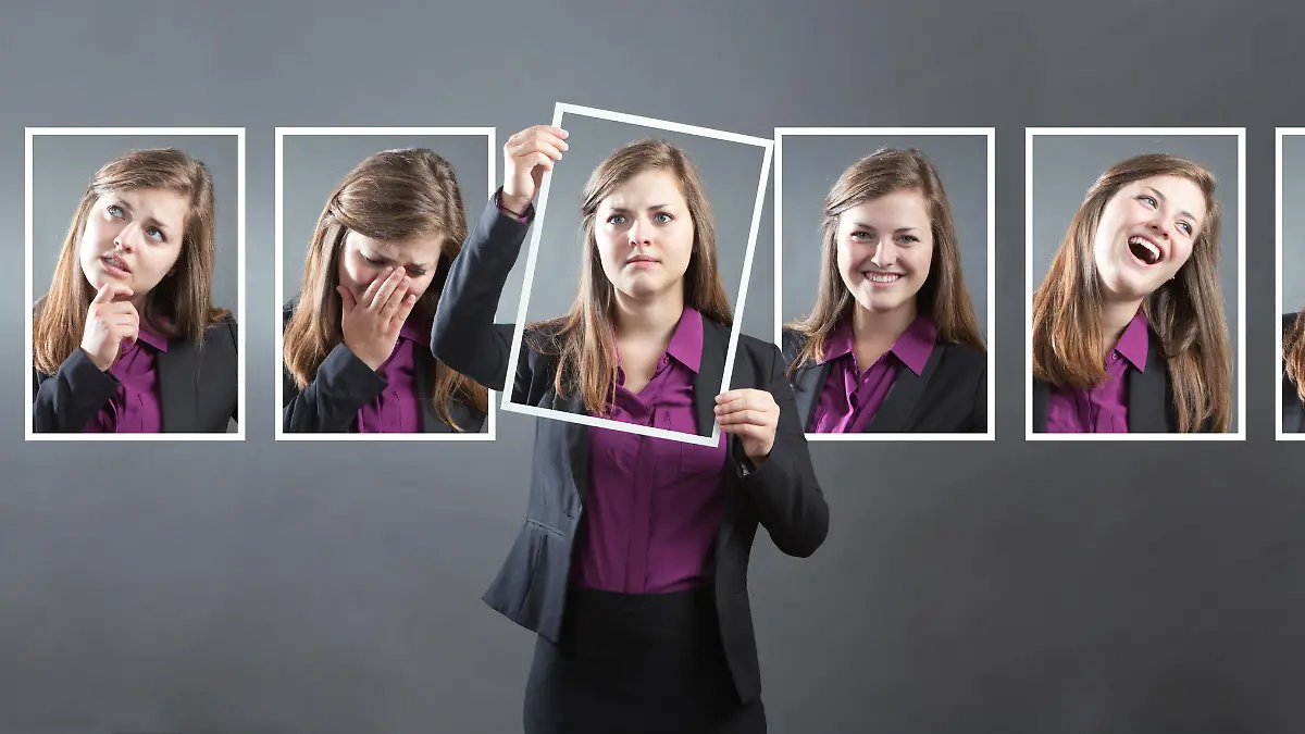 Concept photo for personality, character and emotional expression. A woman in business suit holding up a photo of herself in front of her with various range of emotional expressions exhibited in the background wall behind her. From happiness to sadness, anger to joy, apprehension to confidence. Photographed in panoramic horizontal format in studio.
