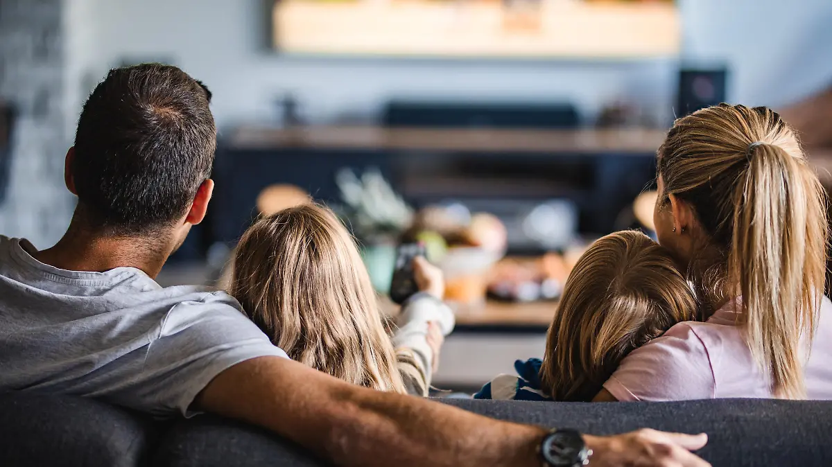 Back view of a relaxed family watching TV on sofa in the living room.