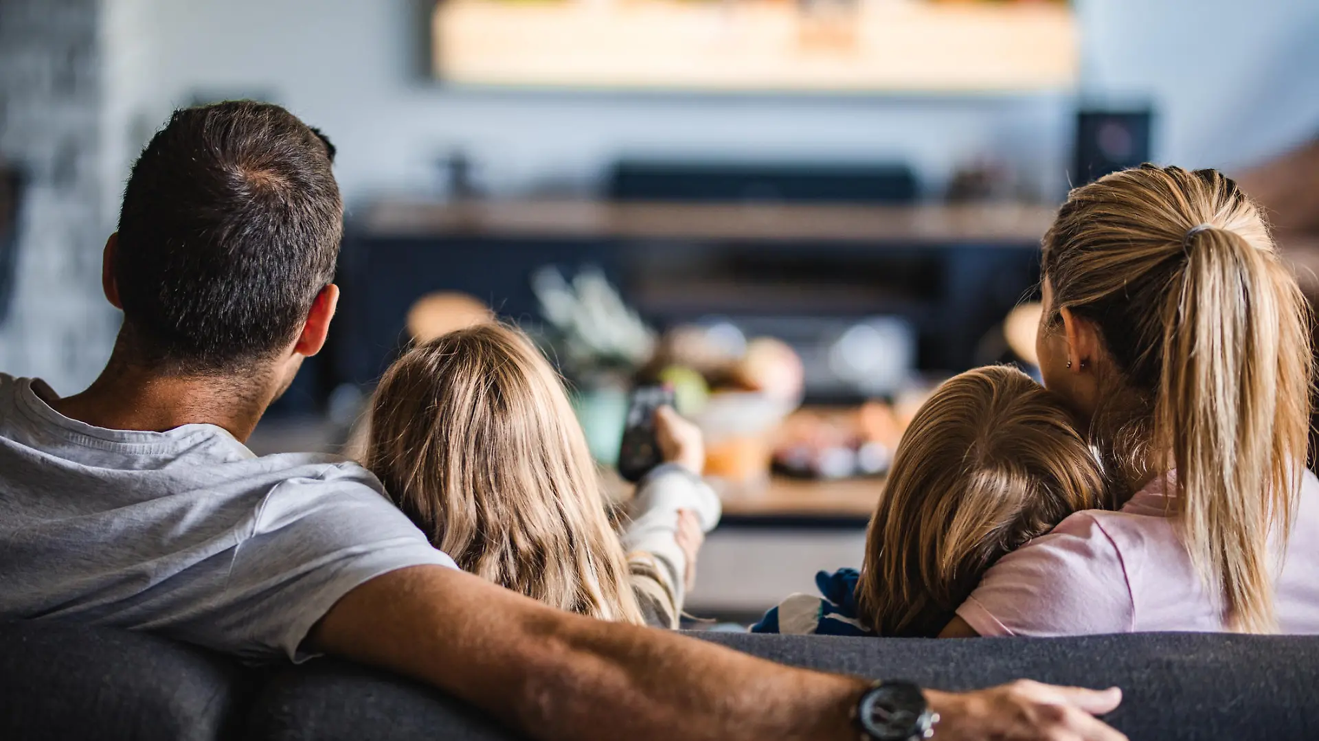 Back view of a relaxed family watching TV on sofa in the living room.