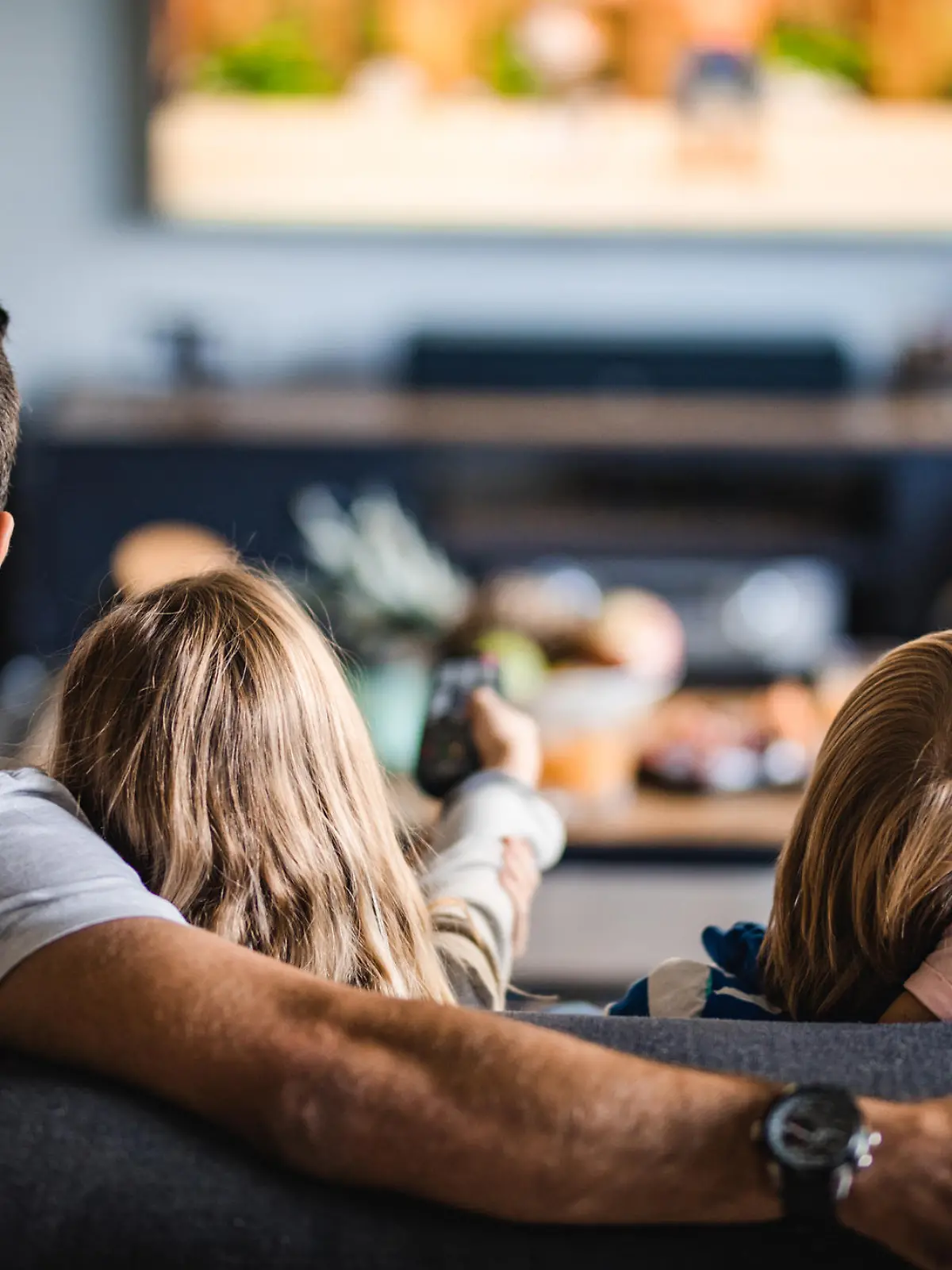 Back view of a relaxed family watching TV on sofa in the living room.