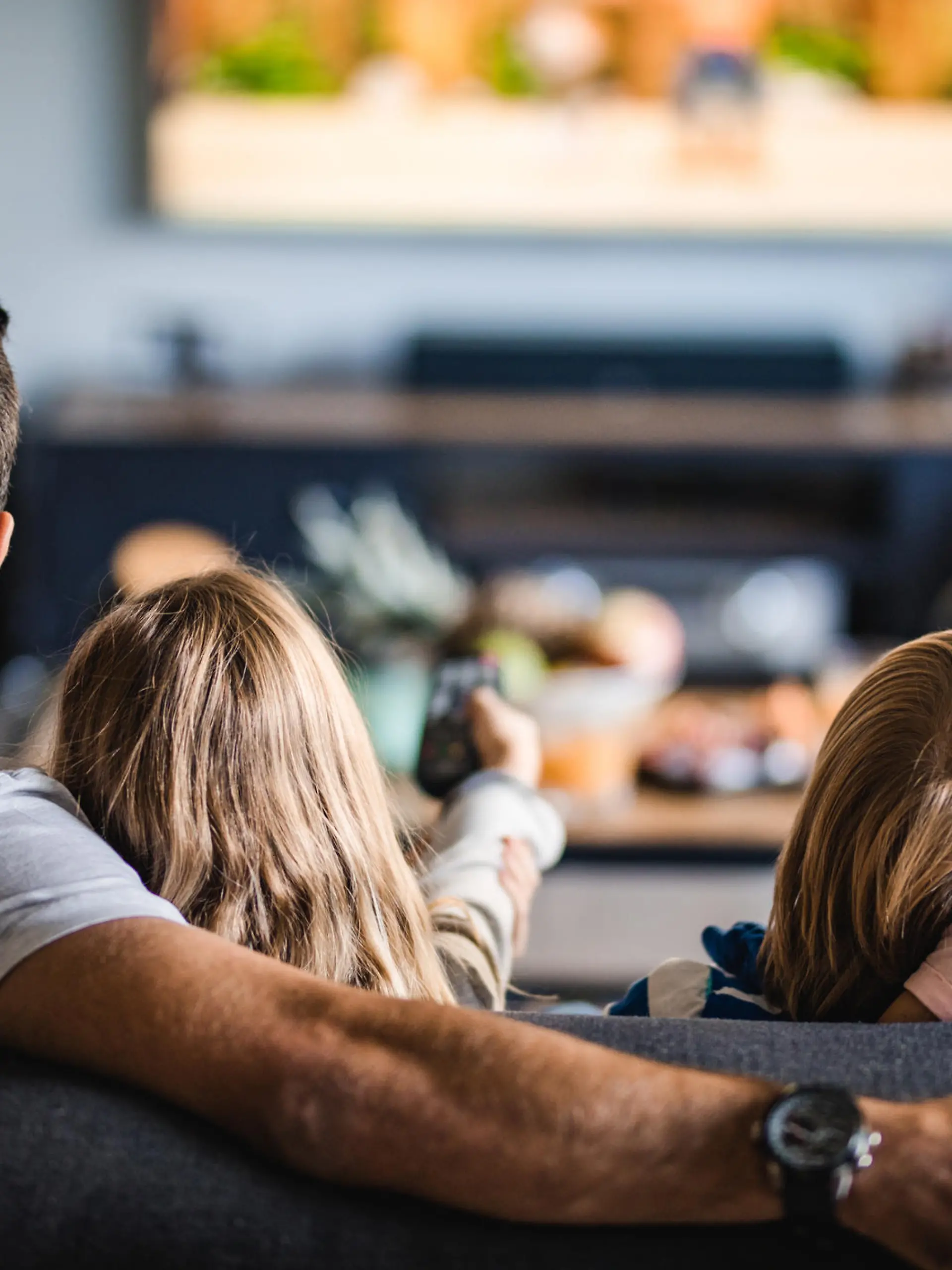 Back view of a relaxed family watching TV on sofa in the living room.
