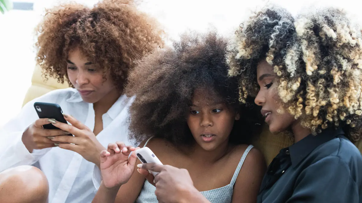 Creative Highlights Symbolbilder Happy African American women and girl using smartphone and smiling while chilling on comfortable couch on weekend day at home together, Model released PauNovell_ThreeAfrosStudio_77.jpg Copyright: xPauxNovellx