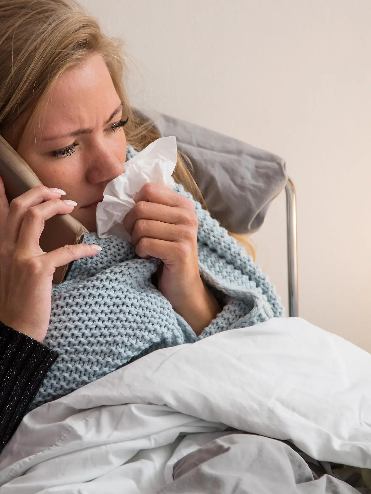 ILLUSTRATION - Eine Frau liegt am 09.10.2019 in Hamburg in einer Wohnung krank im Bett und telefoniert waehrend sie sich die Nase putzt (gestellte Szene). Foto: Christin Klose || Modellfreigabe vorhanden