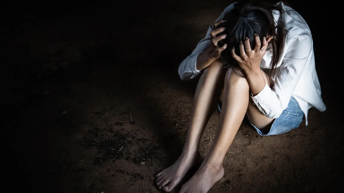 Scared young woman sitting in the corner of her bedroom.
