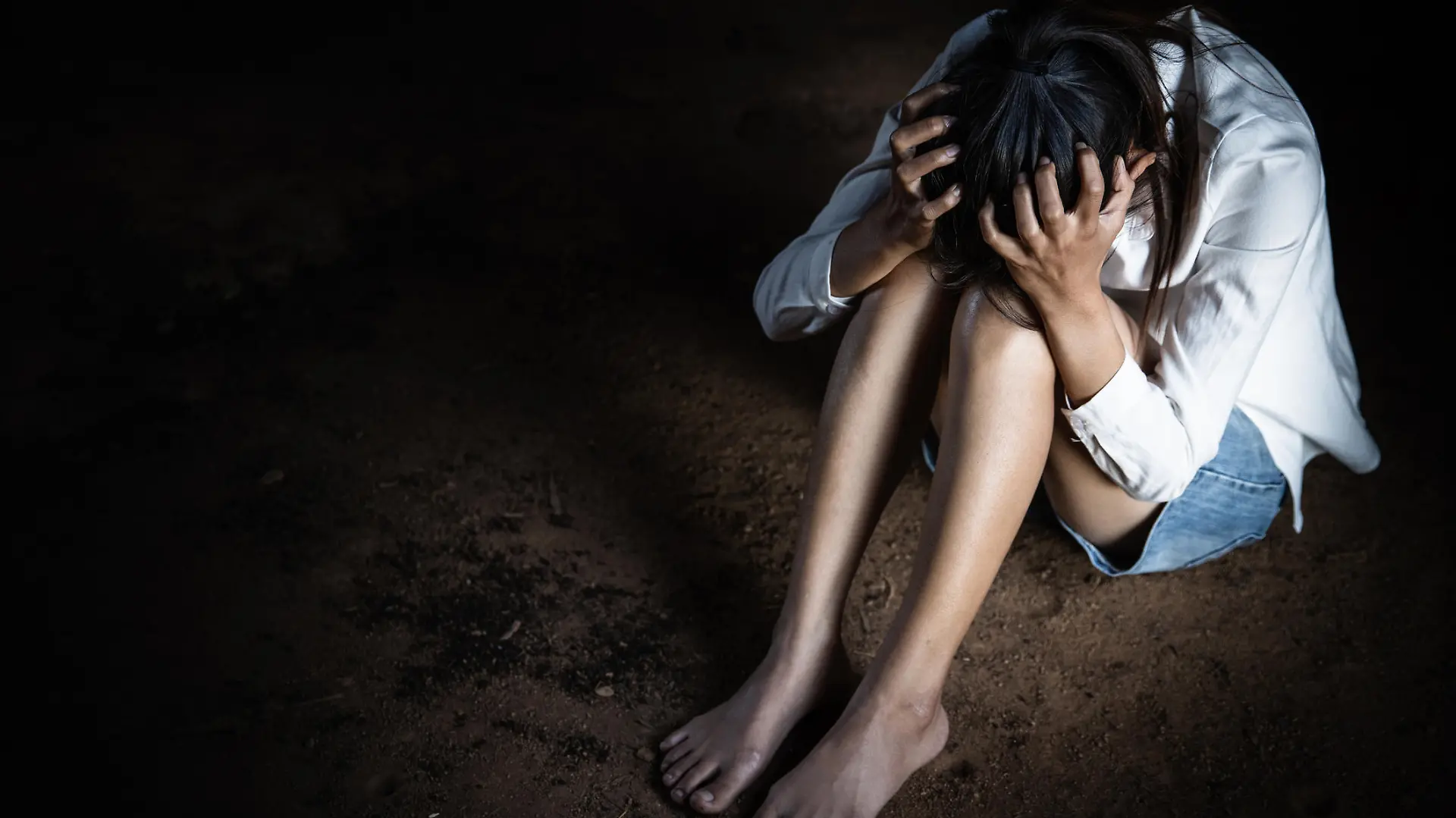 Scared young woman sitting in the corner of her bedroom.