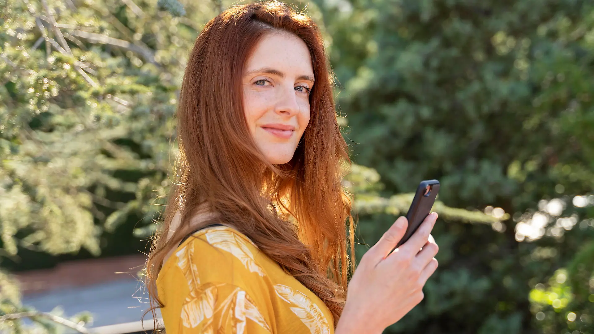 Portrait of smiling redheaded woman with smartphone outdoors model released Symbolfoto AFVF06191