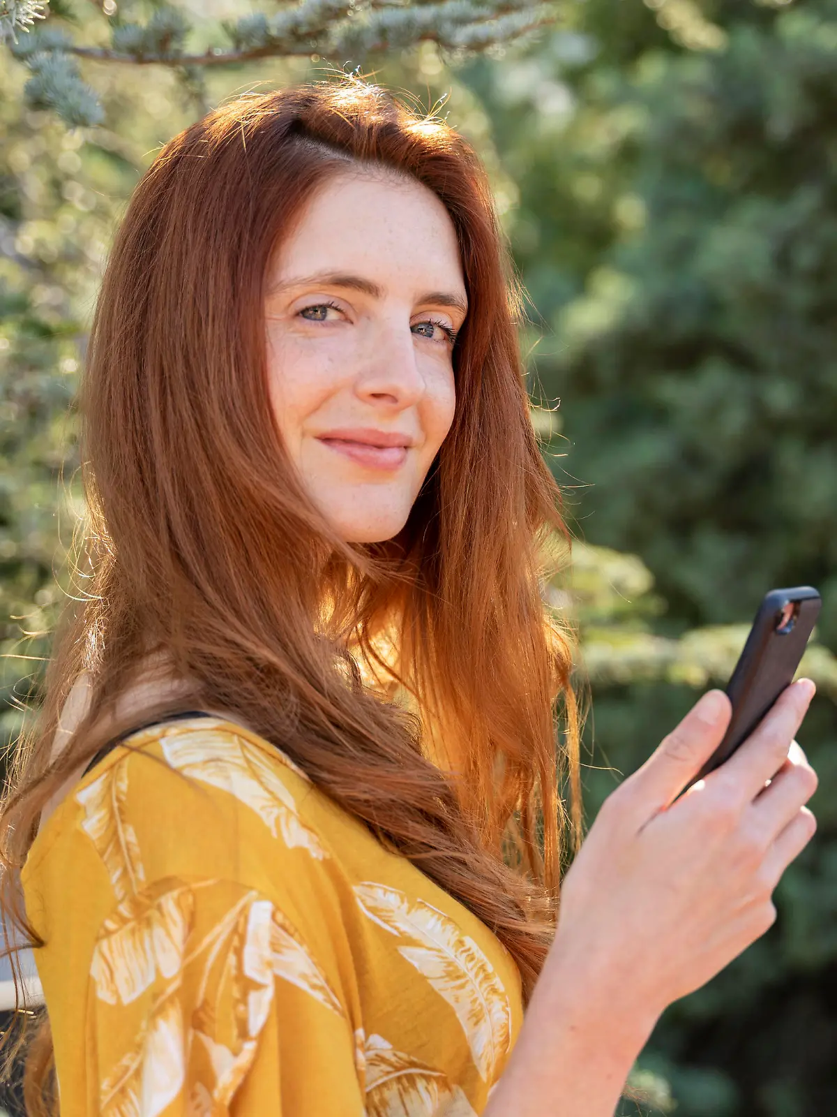  Portrait of smiling redheaded woman with smartphone outdoors model released Symbolfoto AFVF06191