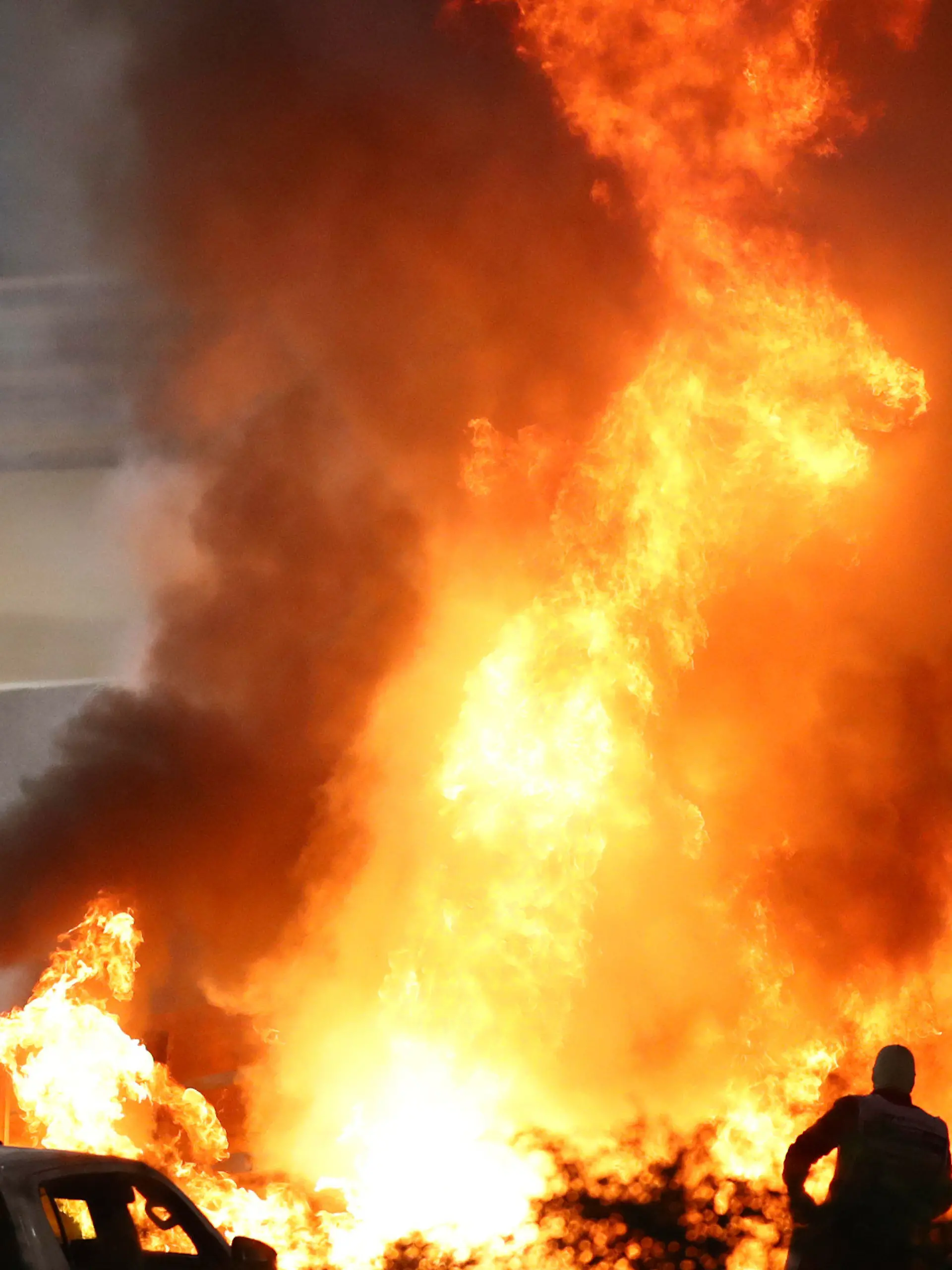FILE - Staff extinguish flames from Haas driver Romain Grosjean's car after a crash during the Formula One race in Bahrain International Circuit in Sakhir, Bahrain, in this Sunday, Nov. 29, 2020, file photo. Mercedes announced Wednesday, May 5, 2021, that Grosjean will drive Lewis Hamilton’s 2019 championship-winning car at the French Grand Prix on June 27 before a full test day at Circuit Paul Ricard two days later. (Brynn Lennon/Pool via AP, File)