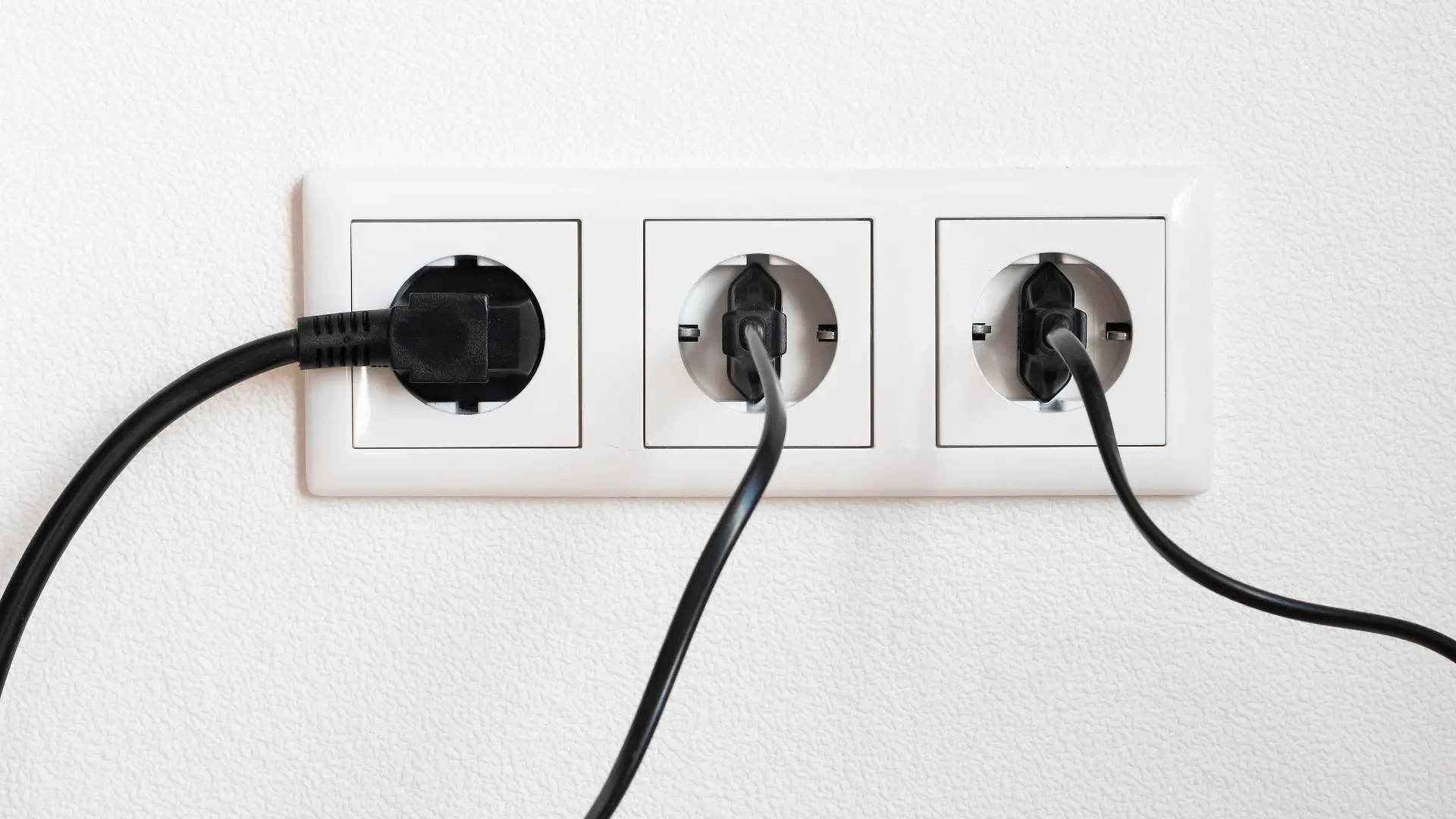 Drei schwarze Stecker in einer weissen dreifach Steckdose