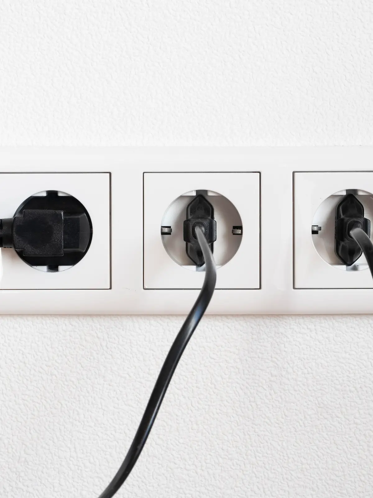 Drei schwarze Stecker in einer weissen dreifach Steckdose