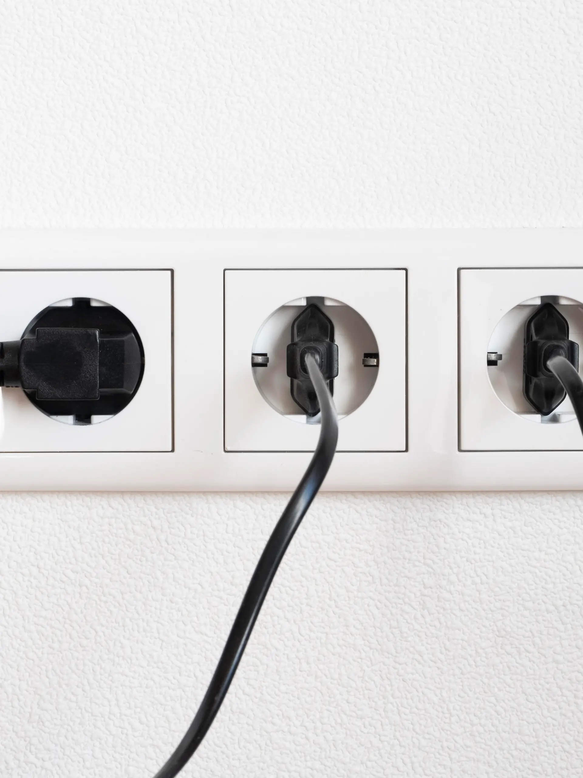 Drei schwarze Stecker in einer weissen dreifach Steckdose