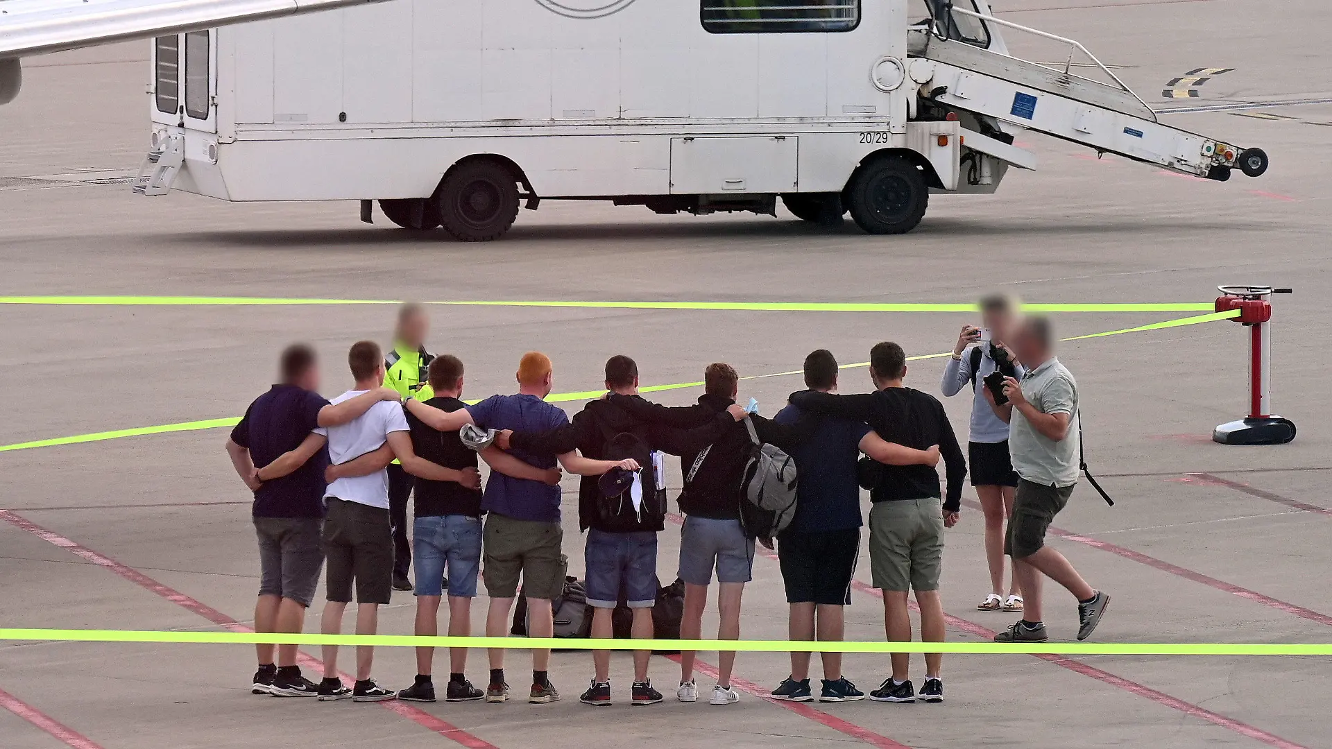 16.07.2022, Nordrhein-Westfalen, Münster: Die acht Männer, die auf Mallorca wegen Brandstiftung in Untersuchungshaft gesessen haben, stehen nach ihrer Ankunft in Deutschland auf dem Flugfeld auf dem Flughafen Münster-Osnabrück zusammen. Die acht Deutschen, die auf Mallorca der Brandstiftung verdächtigt werden und in U-Haft saßen, sind nach knapp zwei Monaten wieder zu Hause im Münsterland. (zu dpa: «Kegelbrüder wieder zu Hause - Mallorca-Alptraum ist aber nicht vorbei») Foto: Helmut P. Etzkorn/dpa - ACHTUNG: Person(en) wurde(n) aus rechtlichen Gründen gepixelt +++ dpa-Bildfunk +++