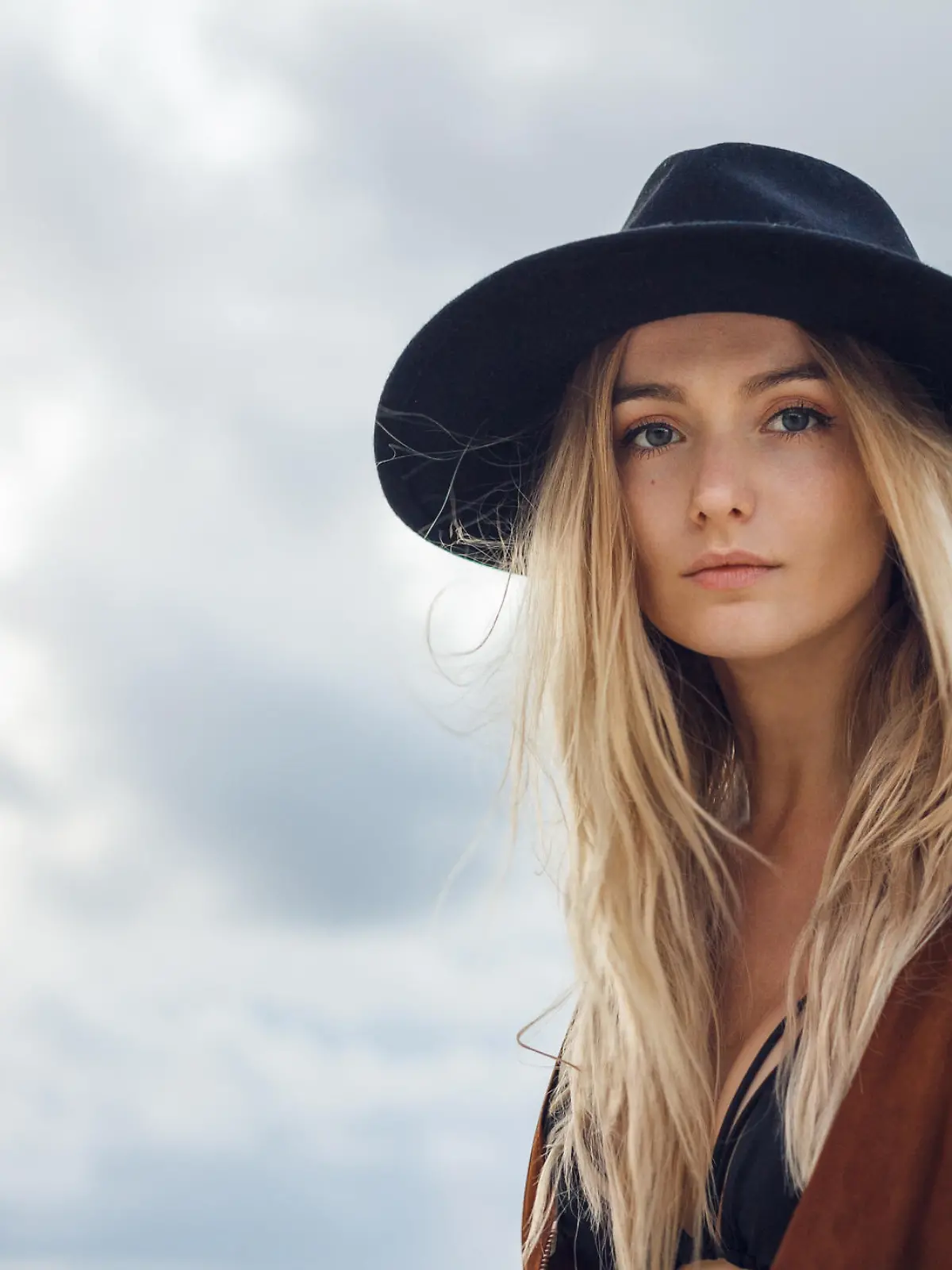 Close up of beautiful young blonde woman with black hat. Wearing brown vest. Her long messy hair looks amazing.