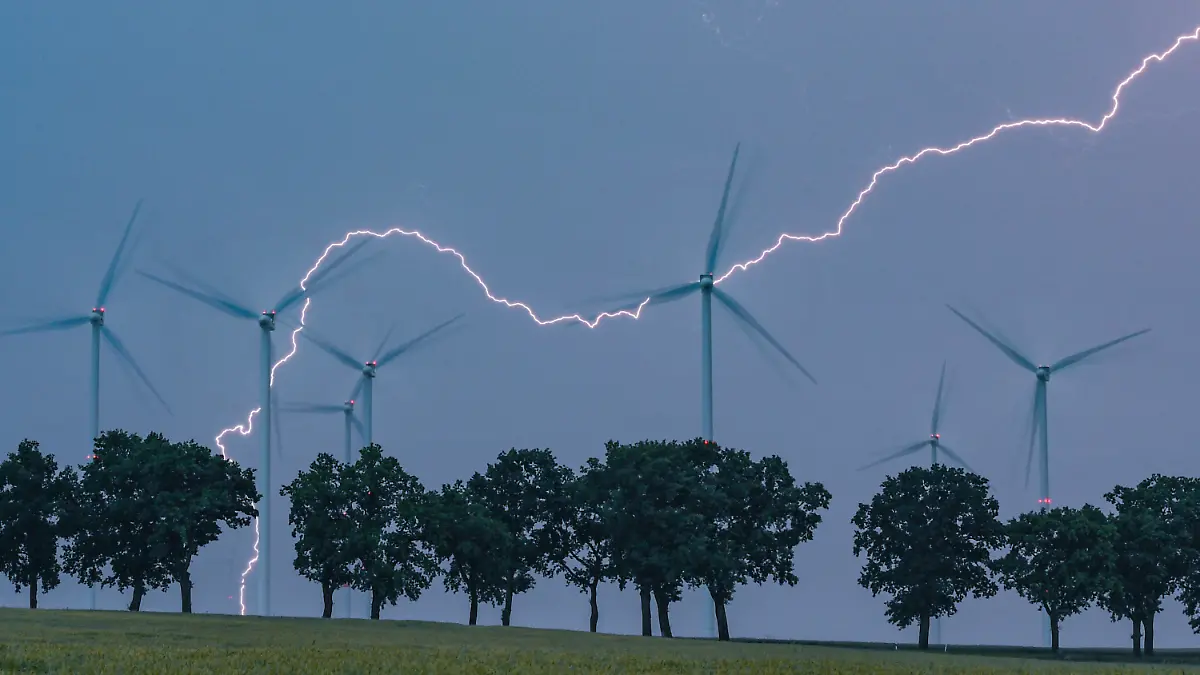 ARCHIV - 13.06.2020, Brandenburg, Petersdorf: Ein Blitz erhellt den Abendhimmel über der Landschaft mit Windenergieanlagen und einer Allee im Landkreis Oder-Spree. In der vergangenen Nacht zogen Gewitter über das Land Brandenburg. (zu "Meteorologe zu Unwettern: «wieder mal ein ganz normaler Sommer»") Foto: Patrick Pleul/dpa-Zentralbild/dpa +++ dpa-Bildfunk +++