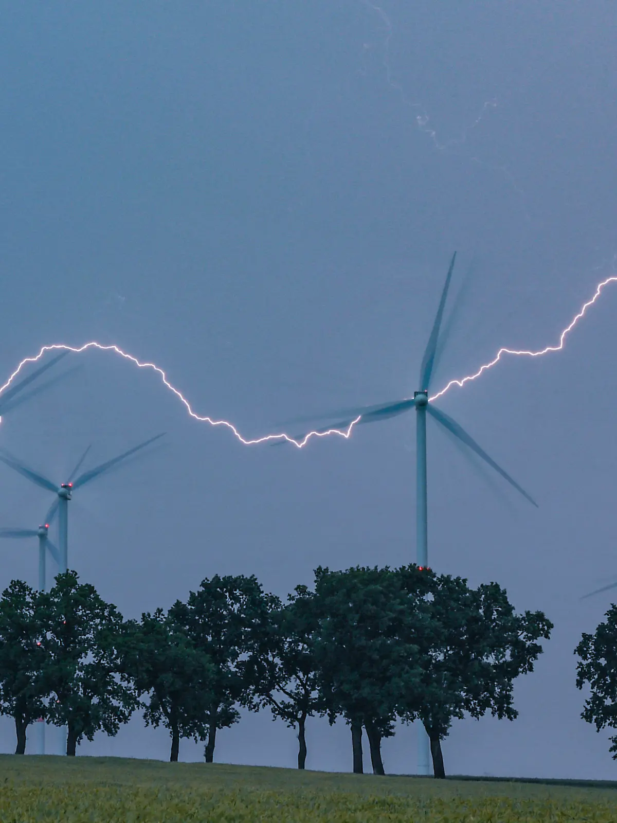 ARCHIV - 13.06.2020, Brandenburg, Petersdorf: Ein Blitz erhellt den Abendhimmel über der Landschaft mit Windenergieanlagen und einer Allee im Landkreis Oder-Spree. In der vergangenen Nacht zogen Gewitter über das Land Brandenburg. (zu "Meteorologe zu Unwettern: «wieder mal ein ganz normaler Sommer»") Foto: Patrick Pleul/dpa-Zentralbild/dpa +++ dpa-Bildfunk +++