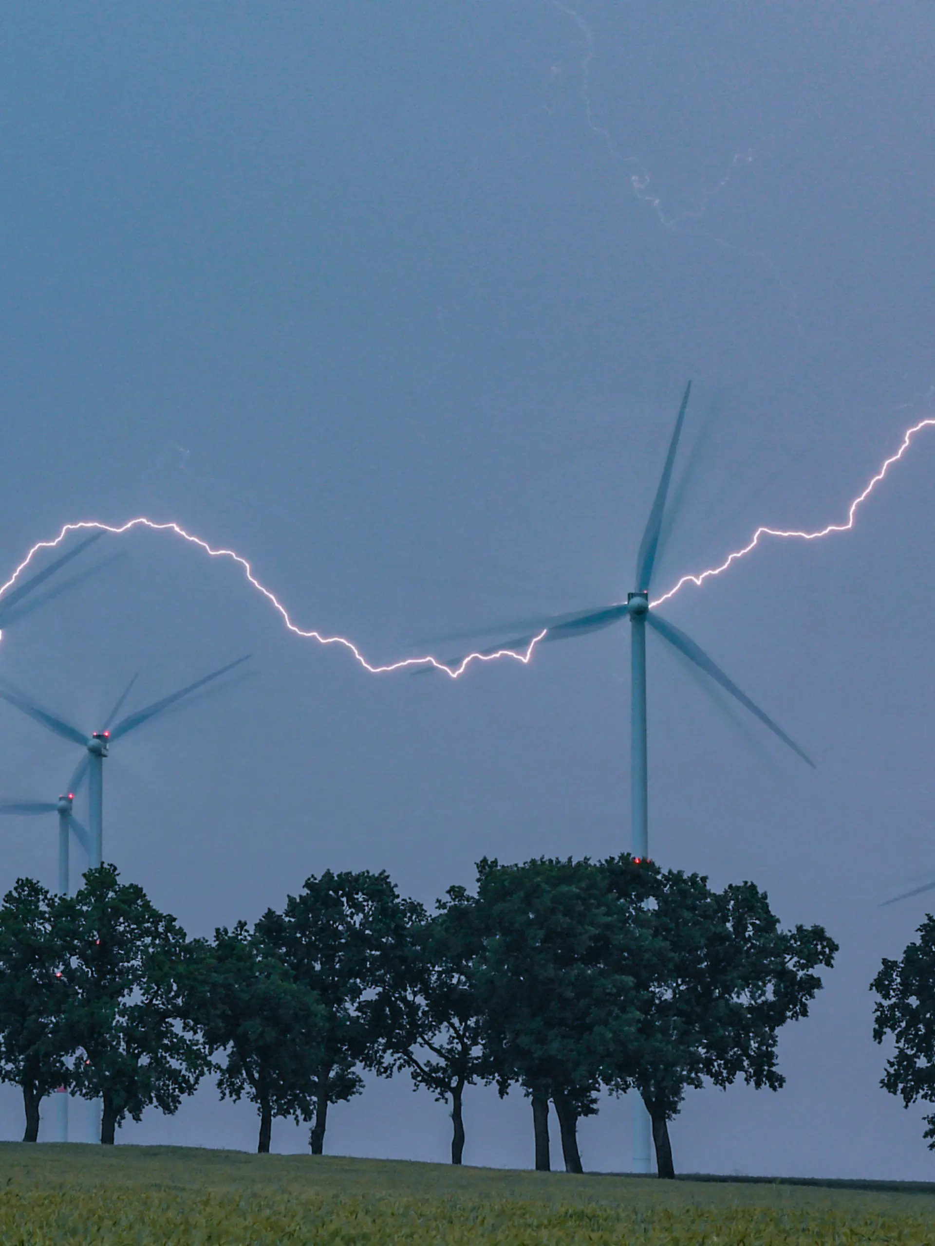 ARCHIV - 13.06.2020, Brandenburg, Petersdorf: Ein Blitz erhellt den Abendhimmel über der Landschaft mit Windenergieanlagen und einer Allee im Landkreis Oder-Spree. In der vergangenen Nacht zogen Gewitter über das Land Brandenburg. (zu "Meteorologe zu Unwettern: «wieder mal ein ganz normaler Sommer»") Foto: Patrick Pleul/dpa-Zentralbild/dpa +++ dpa-Bildfunk +++