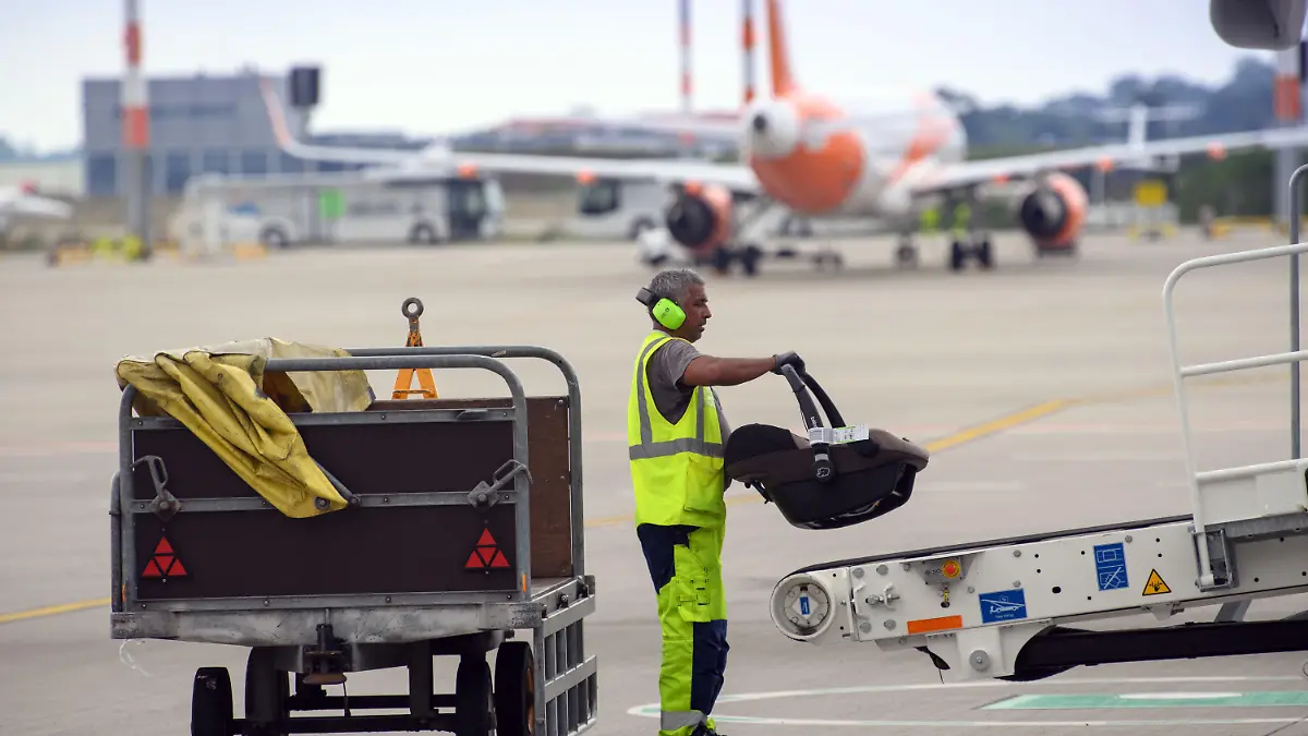 ARCHIV - 14.07.2021, Brandenburg, Schönefeld: Ein Mitarbeiter der WISAG Aviation lädt auf dem Vorfeld des Flughafen BER ·Willy Brandt· einen Kindersitz auf das Gepäck-Transportband (Power Stow) am Flugzeug. Wegen des Chaos im europäischen Luftverkehr sind die Arbeitsbedingungen der Branche ins Blickfeld gerückt. Bundesverkehrsminister Wissing sprach sich in einem Interview am Montag (04.07.2022) für eine angemessene Bezahlung aus. Foto: Soeren Stache/dpa-Zentralbild/dpa +++ dpa-Bildfunk +++