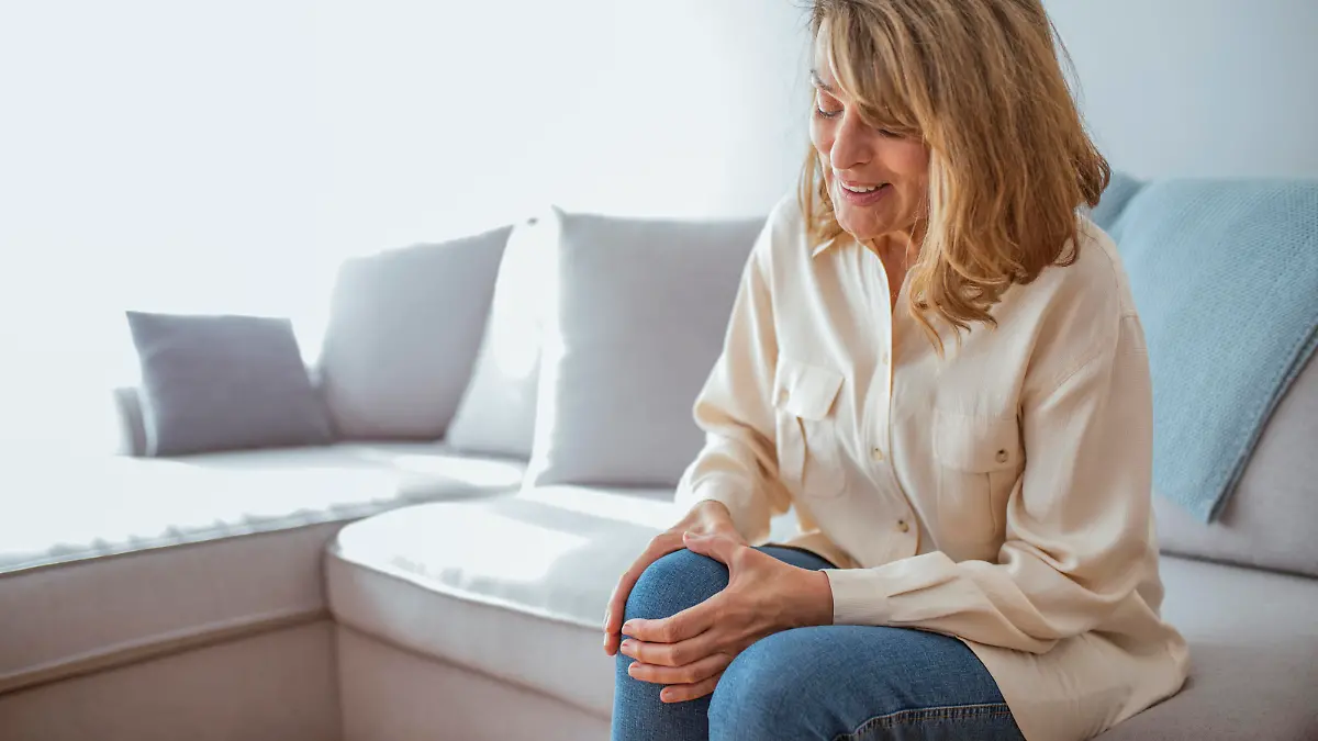 Old age, health problem and people concept - senior woman suffering from pain in leg at home. Health care concept. A woman suffering from pain in the knee, closeup. Old age, health problem and people concept - senior woman suffering from pain in leg at home. Photo of Senior woman holding the knee with the pain while sitting on the sofa during the day.