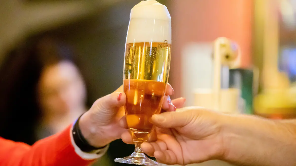ARCHIV - 06.12.2021, Berlin: Ein Kneipenwirt reicht in einer Berliner Gaststätte einem Gast ein Bier. Menschen unter 40 Jahre sollten einer neuen Studie zufolge deutlich weniger Alkohol trinken als bisher angenommen. (zu dpa «Studie: Mehr als ein winziges Bier pro Tag schadet unter 40-Jährigen») Foto: Christoph Soeder/dpa +++ dpa-Bildfunk +++