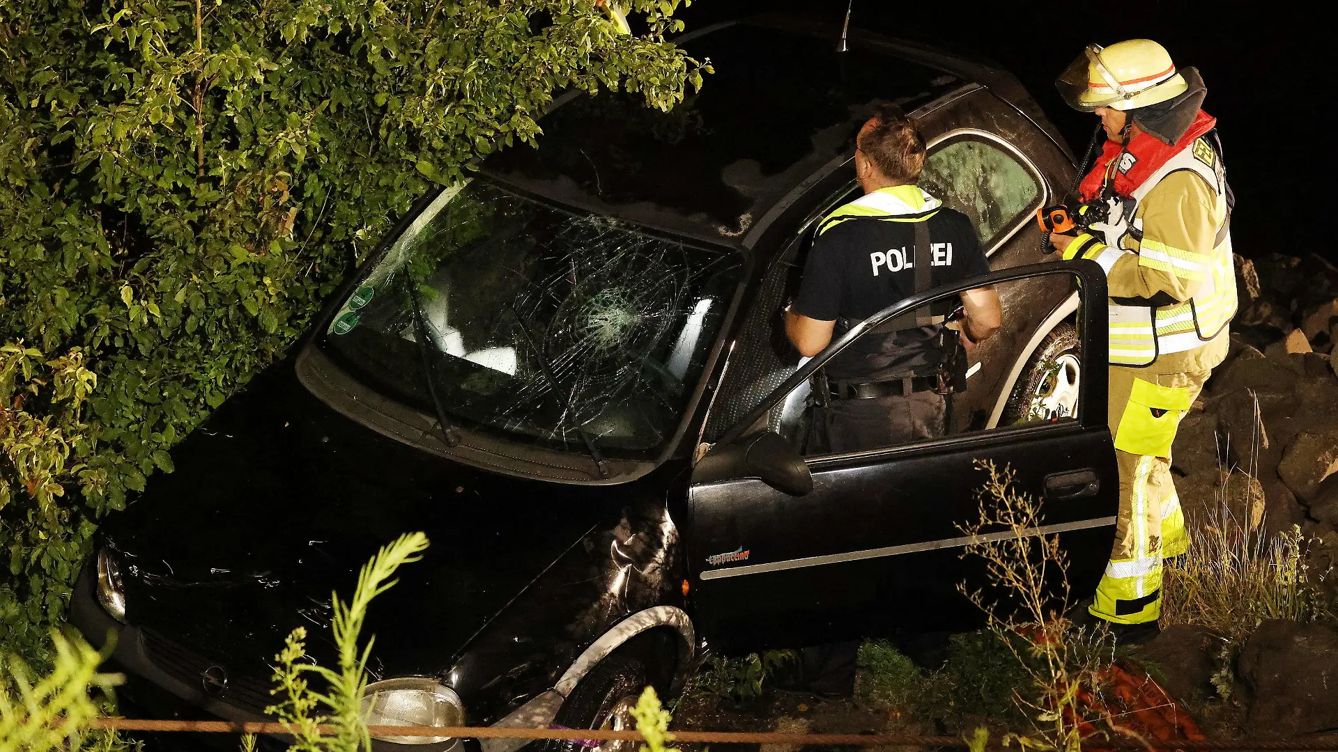 16.07.2022, Nordrhein-Westfalen, Düsseldorf: Polizisten und Feuerwehrleute arbeiten an einem geborgenen Opel Corsa. Eine 23 Jahre alte Fahrerin hat bei einem missglückten Wendemanöver versehentlich das falsche Pedal getreten. Das Auto sei vom Parkplatz direkt in den Rhein gefahren und komplett versunken. Foto: David Young/dpa +++ dpa-Bildfunk +++