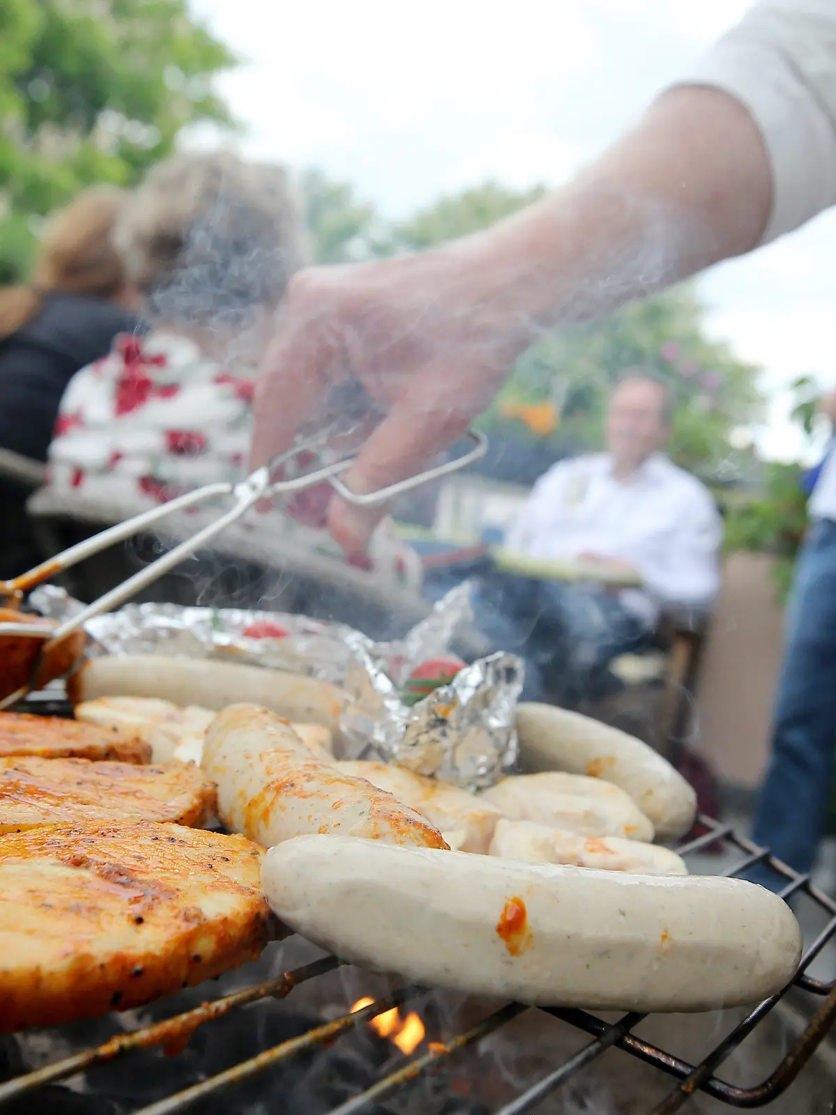 ARCHIV - Ein Partygast wendet am 13.05.2017 in Essen (Nordrhein-Westfalen) Grillgut auf einem kleinen Rundgrill. (zu dpa "Festmahl oder Wurst-Case-Szenario? Vom guten und schlechten Grillen" vom 23.05.2017) Foto: Roland Weihrauch/dpa +++(c) dpa - Bildfunk+++