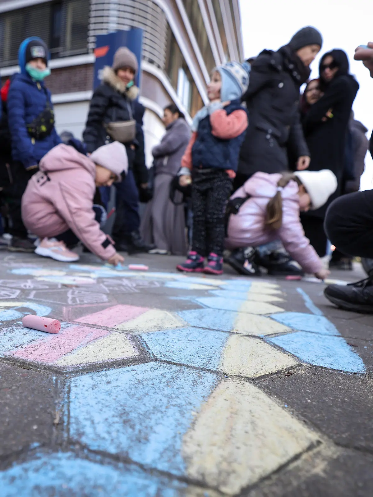 ARCHIV - 09.03.2022, Hamburg: Kinder, die mit ihren Angehörigen aus der Ukraine geflohen sind, malen mit Kreide auf den Boden, während ihre Familien und weiterer ukrainische Flüchtlinge vor der Zentralen Ausländerbehörde mit der neuen Registrierungsstelle im Amt für Migration an der Hammer Straße warten. (zu dpa «Hamburg stellt sich auf Tausende neue Schüler aus der Ukraine ein») Foto: Christian Charisius/dpa +++ dpa-Bildfunk +++