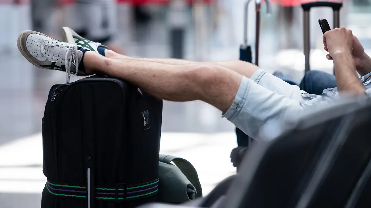 02.07.2022, Nordrhein-Westfalen, Düsseldorf: Ein Mann sitzt in der Abflughalle des Flughafens und hat seine Beine auf seinem Koffer abgelegt. Eine Woche nach Start der Sommerferien hat sich die Lage an den Flughäfen in Nordrhein-Westfalen deutlich entspannt. Foto: Marius Becker/dpa +++ dpa-Bildfunk +++