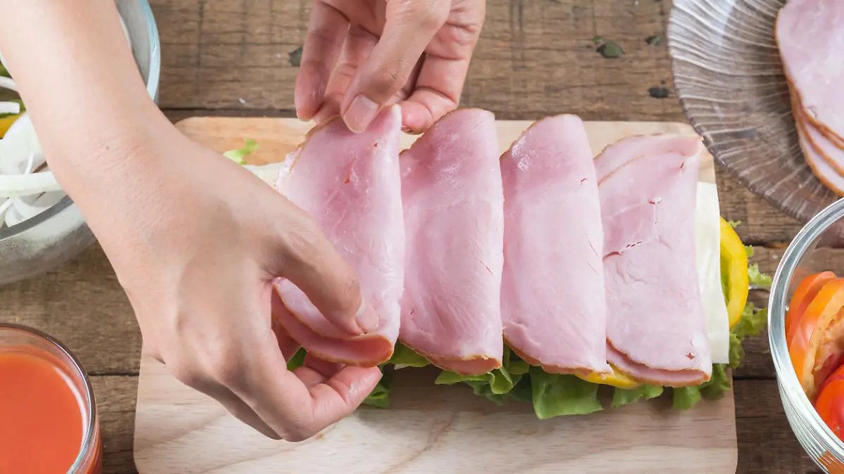 Making baguette ham sandwich, woman's hands placing ham on baguette sandwich