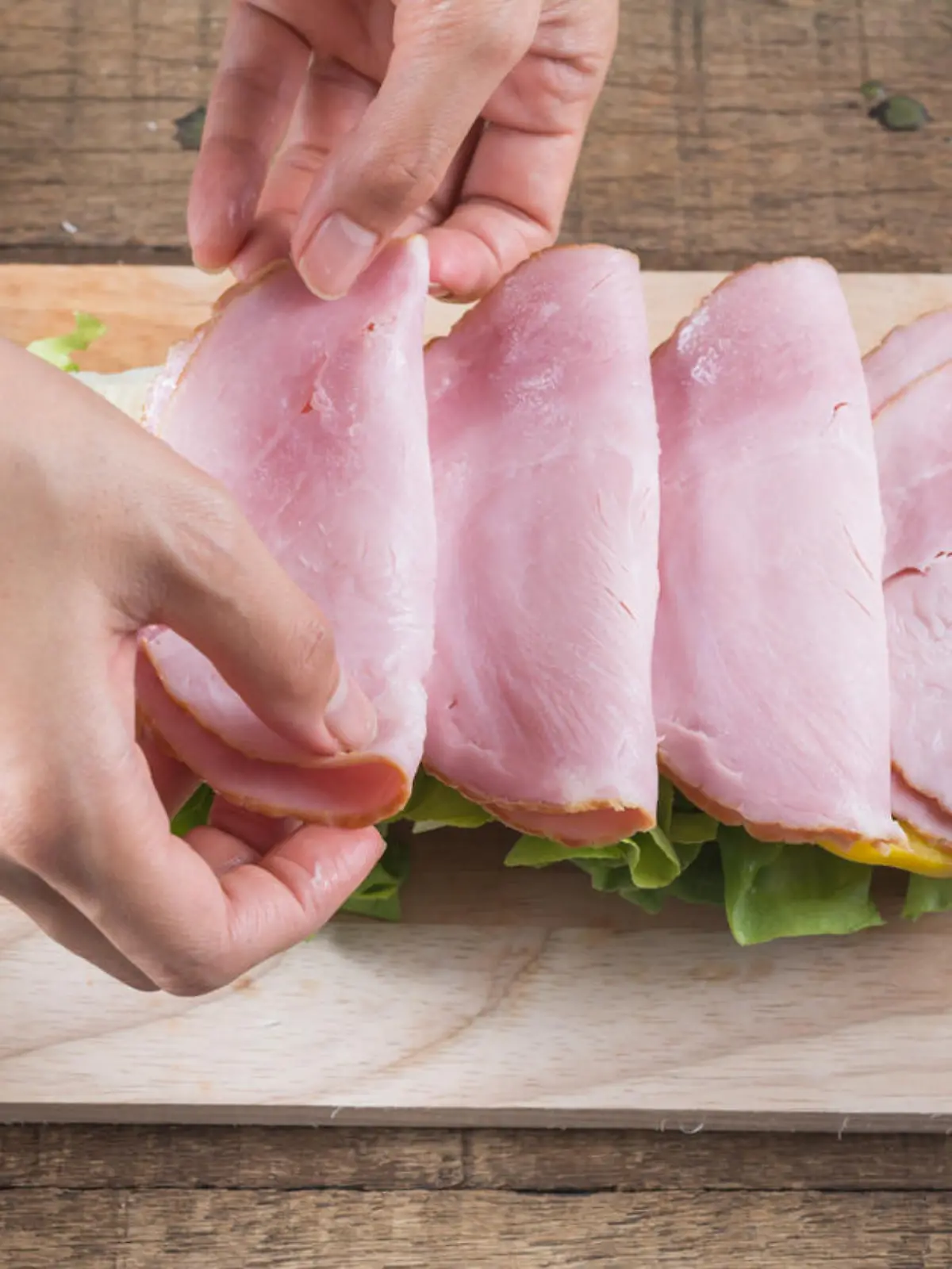 Making baguette ham sandwich, woman's hands placing ham on baguette sandwich