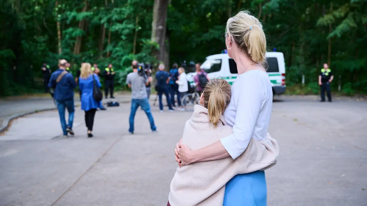 dpatopbilder - 20.07.2023, Brandenburg, Kleinmachnow: Eine Anwohnerin und ihre Tochter sehen dem Treiben von Journalisten und Polizei zu, während Tierexperten und Polizeibeamten in einem Waldgebiet in Zehlendorf stehen. Eine freilaufende Raubkatze soll in der Gemeinde Kleinmachnow in Brandenburg gesichtet worden sein. Foto: Annette Riedl/dpa +++ dpa-Bildfunk +++