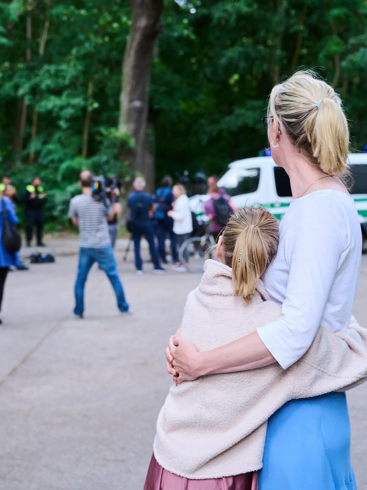 dpatopbilder - 20.07.2023, Brandenburg, Kleinmachnow: Eine Anwohnerin und ihre Tochter sehen dem Treiben von Journalisten und Polizei zu, während Tierexperten und Polizeibeamten in einem Waldgebiet in Zehlendorf stehen. Eine freilaufende Raubkatze soll in der Gemeinde Kleinmachnow in Brandenburg gesichtet worden sein. Foto: Annette Riedl/dpa +++ dpa-Bildfunk +++