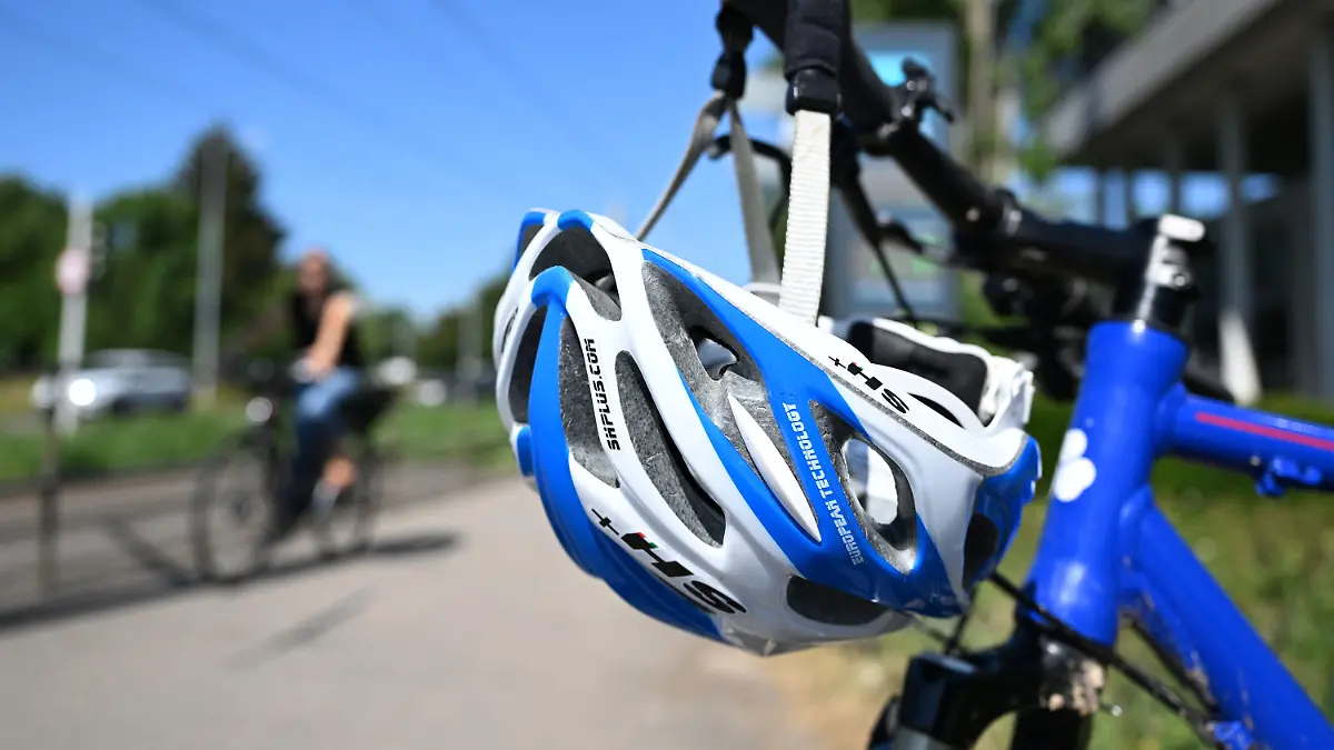 ILLUSTRATION - 30.06.2022, Baden-Württemberg, Stuttgart: Ein Helm hängt an einem Lenker an einem Fahrrad (gestellte Szene). Die Mehrheit der Menschen in Deutschland spricht sich für eine Helmpflicht für Fahrradfahrinnen und Fahrradfahrer aus. Das ist das Ergebnis einer aktuellen bundesweiten Umfrage des Instituts Forsa im Auftrag der Prüf- und Expertenorganisation Dekra. Foto: Bernd Weißbrod/dpa +++ dpa-Bildfunk +++