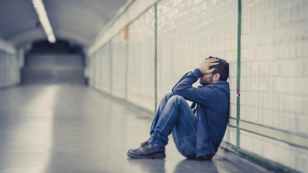 Young man abandoned lost in depression sitting on ground street subway tunnel suffering emotional pain, sadness and looking destroyed and desperate leaning on wall alone