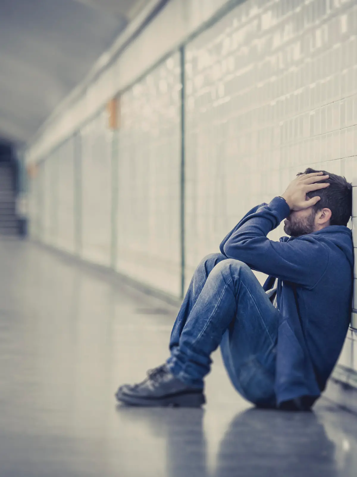 Young man abandoned lost in depression sitting on ground street subway tunnel suffering emotional pain, sadness and looking destroyed and desperate leaning on wall alone 