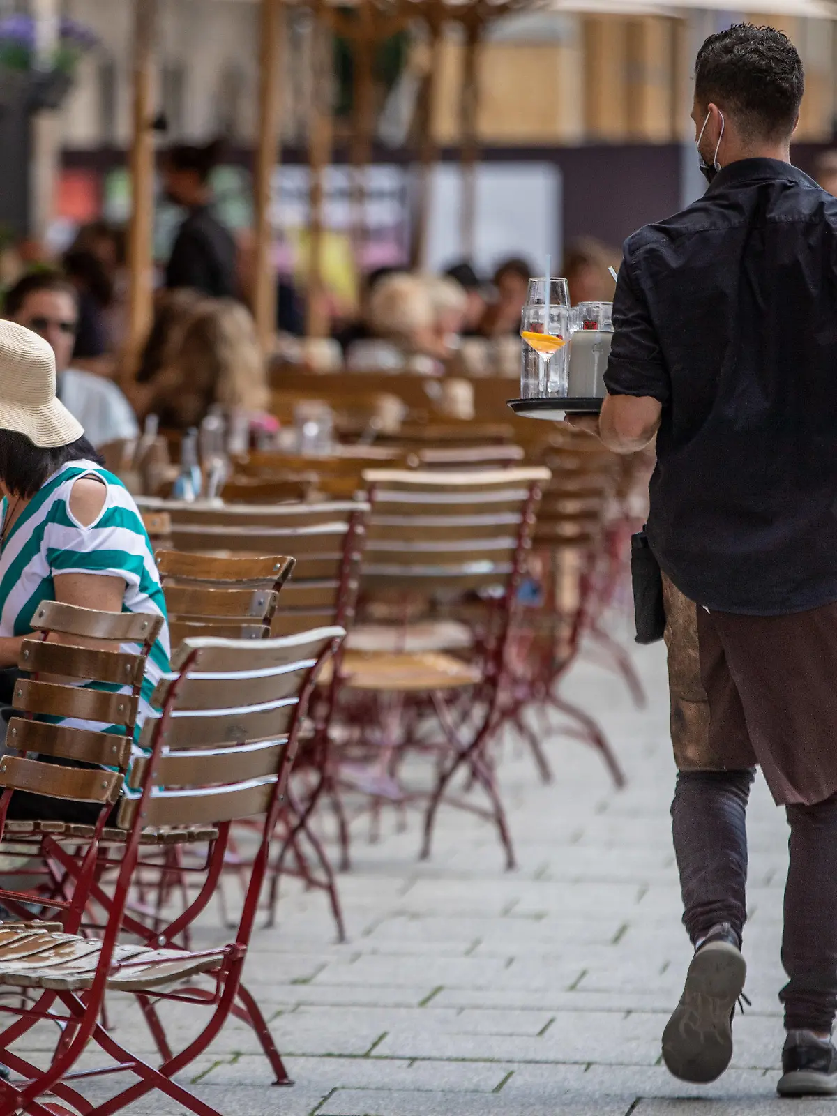 ARCHIV - 20.08.2021, Baden-Württemberg, Stuttgart: Eine Servicekraft läuft im Außenbereich eines Restaurants an Gästen vorbei. Experten im Gastgewerbe und der Landwirtschaft sehen die Ausstattung mit Saisonkräften in Sachsen-Anhalt in den jeweiligen Branchen verbessert. (zu dpa: «Verbände sehen Situation mit Saisonkräften verbessert») Foto: Christoph Schmidt/dpa +++ dpa-Bildfunk +++